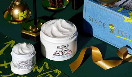 Koyu yeşil bir arka plan uzerinde altın detaylarla yerleştirilmiş bir grafik, iki acık beyaz kavanozu ve icerideki urun kıvrımlarını sergiliyor. Daha kucuk kavanoz "KIEHL’S ULTRA FACIAL CREAM," daha buyuk kavanoz ise "KIEHL’S ULTRA BODY MEGA MOISTURE SQUALANE CREAM" olarak belirtilmiş. Arka planda ise uzerinde altın harflerle "SINCE 1851" yazan mavi bir Kiehl’s hediye kutusu, altın bir kurdele, altın bir teraziyle bir sus eşyası ve kucuk bir cam kozalağı yer alıyor.