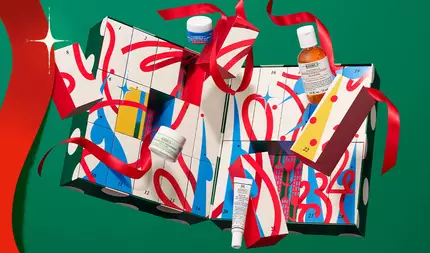 Kiehl’s holiday advent calendar with numbered gift boxes and skincare products, wrapped in red ribbon on a festive green background. ​