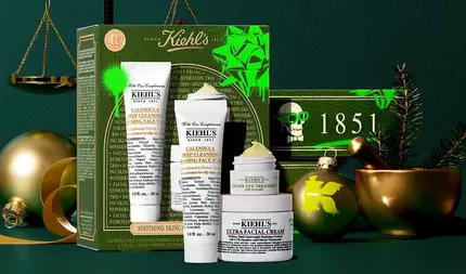 Kiehl’s hediye seti, altın suslemeler, altın terazi ve yeşil dallarla suslenmiş şenlikli bir yeşil arka plan onunde sergileniyor. Set, yeşil ve altın detaylara, neon yeşil aksanlara ve Kiehl’s logosuna sahip bir kutunun onunde duzenlenmiş uc urunden oluşuyor: Calendula Deep Cleansing Foaming Face Wash, Creamy Eye Treatment with Avocado ve Ultra Facial Cream. Fon kısmında, '1851' yazısını ve bir kafatası tasarımını iceren yeşil bir kutu gorunerek yılbaşı temasını tamamlıyor.