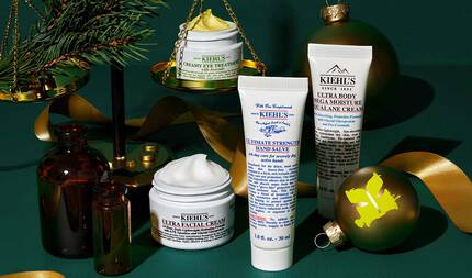 Koyu yeşil dokulu bir arka plan uzerine yerleştirilen şık bir grafik, Kiehl’s urunlerini ve tatil suslerini one cıkarıyor. Soluk sarı kremi gorunen acık beyaz "KIEHL’S CREAMY EYE TREATMENT WITH AVOCADO" kavanozu, altın bir terazinin uzerinde bir cam dalıyla dengelenmiş. Beyaz kremi gorunen beyaz "KIEHL’S ULTRA FACIAL CREAM" kavanozu, beyaz tupte "KIEHL’S ULTIMATE STRENGTH HAND SALVE" ve beyaz tupte "KIEHL’S ULTRA BODY MEGA MOISTURE SQUALANE CREAM" yuzey uzerinde duzenlenmiş. İki kehribar cam şişe, altın bir kurdele ve uzerinde sarı bir “K” logosu bulunan altın bir yuvarlak sus de bu şenlikli tasarımın bir parcası.