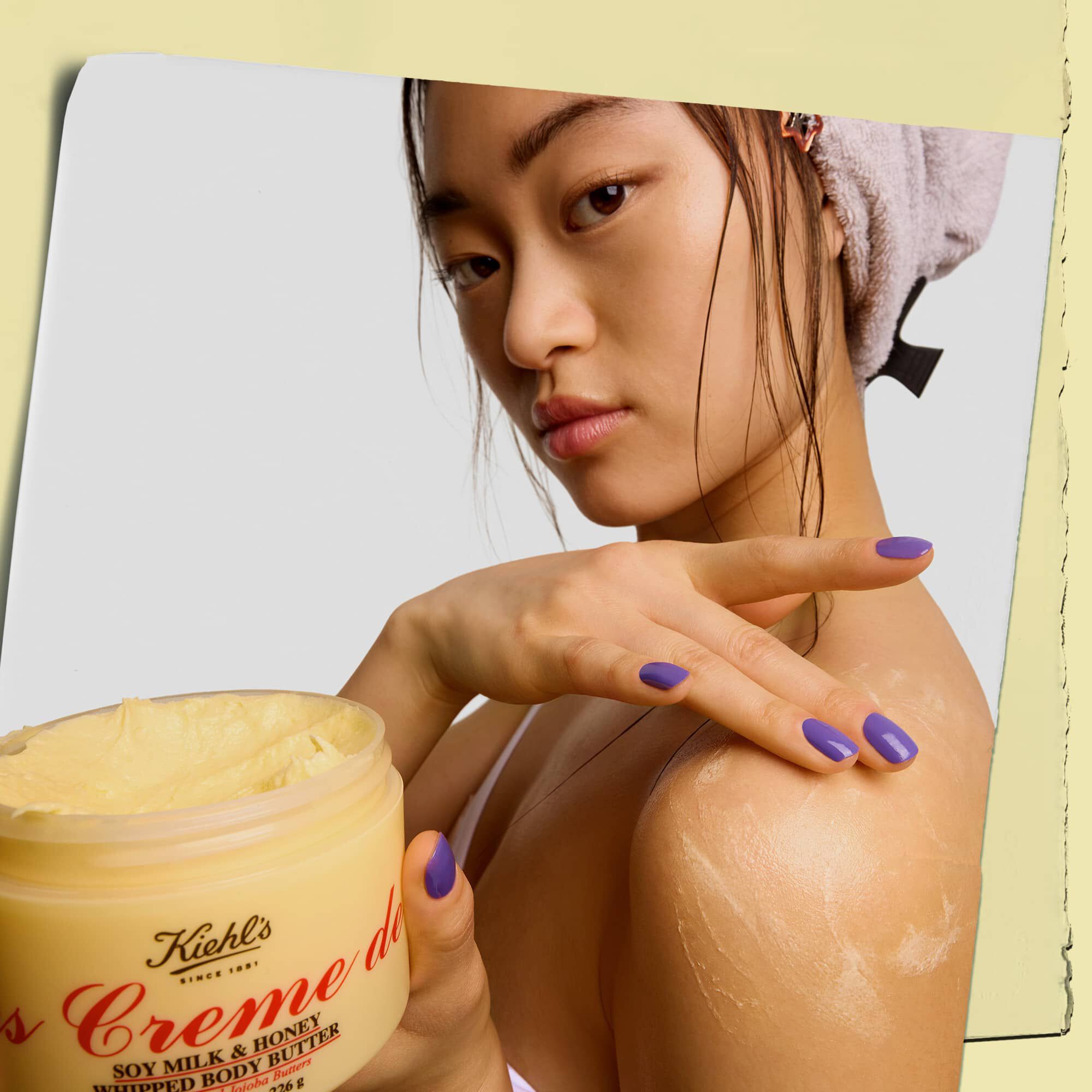 Model, Kiehl's Creme de Corps Whipped Butter Body Butter urununu tutuyor ve uyguluyor.