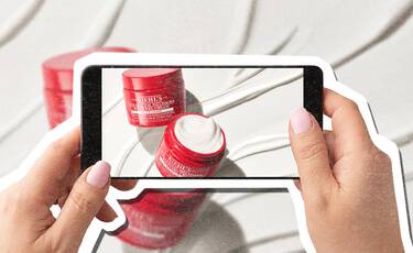 Smartphone photographing red Kiehl’s Super Multi- Corrective Cream jars against a white textured background.