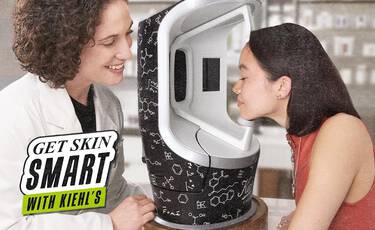 A customer receiving a professional skin analysis using a high-tech diagnostic device with a Kiehl’s skincare expert with the banner "GET SKIN SMART WITH KIEHL'S"