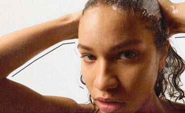Close- up of a woman with wet, curly hair looking directly at the camera while rinsing her hair, illustrating Kiehl’s haircare and personal care products.